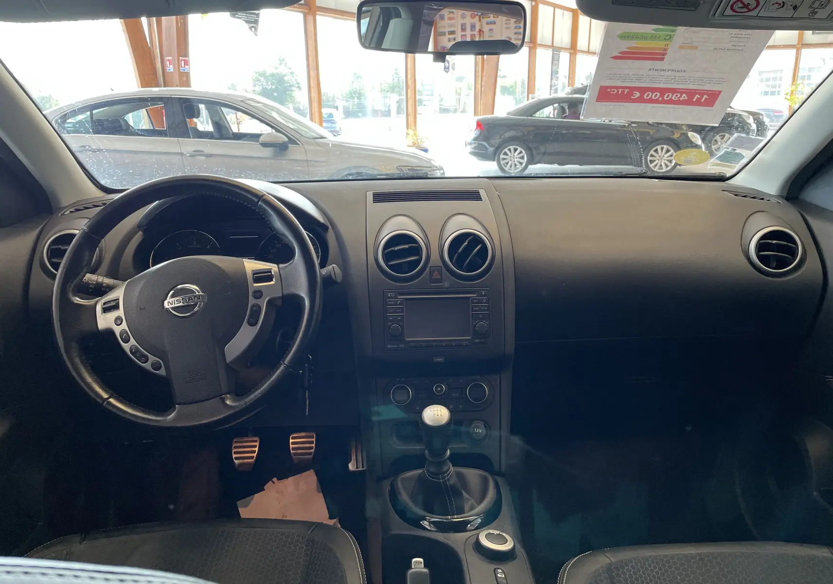 Intérieur noir du Nissan Qashqai 2013, vue frontale du tableau de bord avec volant multifonction et levier de vitesse manuel.