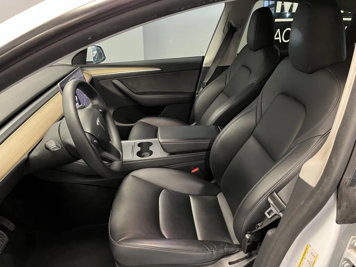 Intérieur noir de la Tesla Model Y RWD 2022 vu côté conducteur, avec tableau de bord bois clair et volant multifonction.