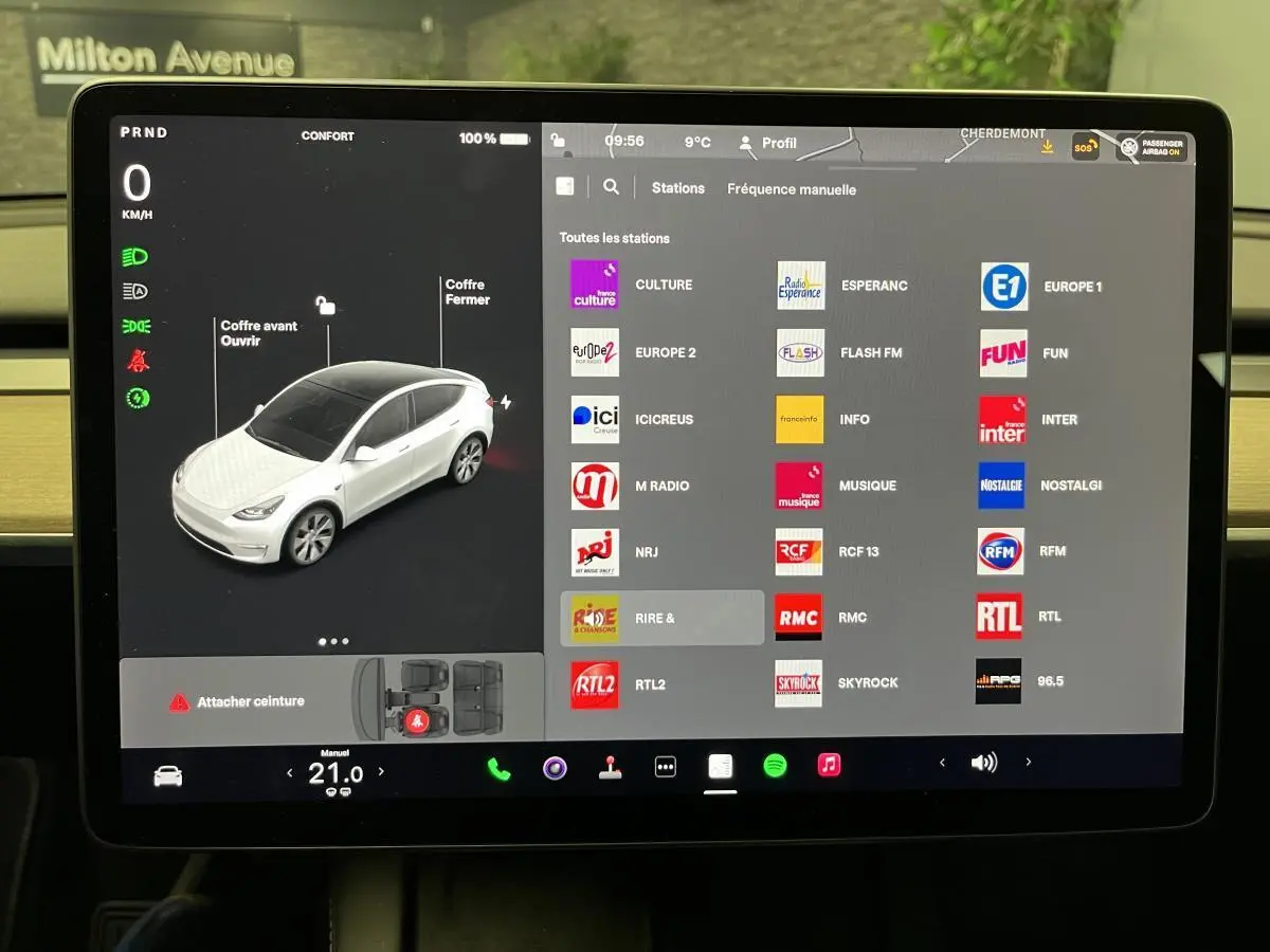 Écran tactile central affichant la Tesla Model Y blanche vue en 3/4 avant avec commandes et stations radio.