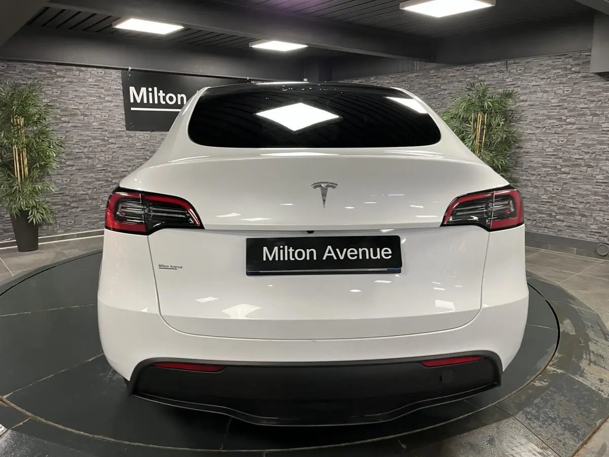 Vue arrière d'une Tesla Model Y blanche nacrée avec vitres teintées et logo Tesla visible sur le hayon.