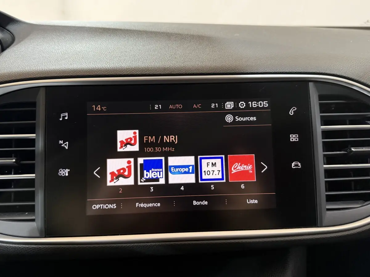 Écran tactile central allumé affichant les stations radio dans l’habitacle d’une Peugeot 308 noire.