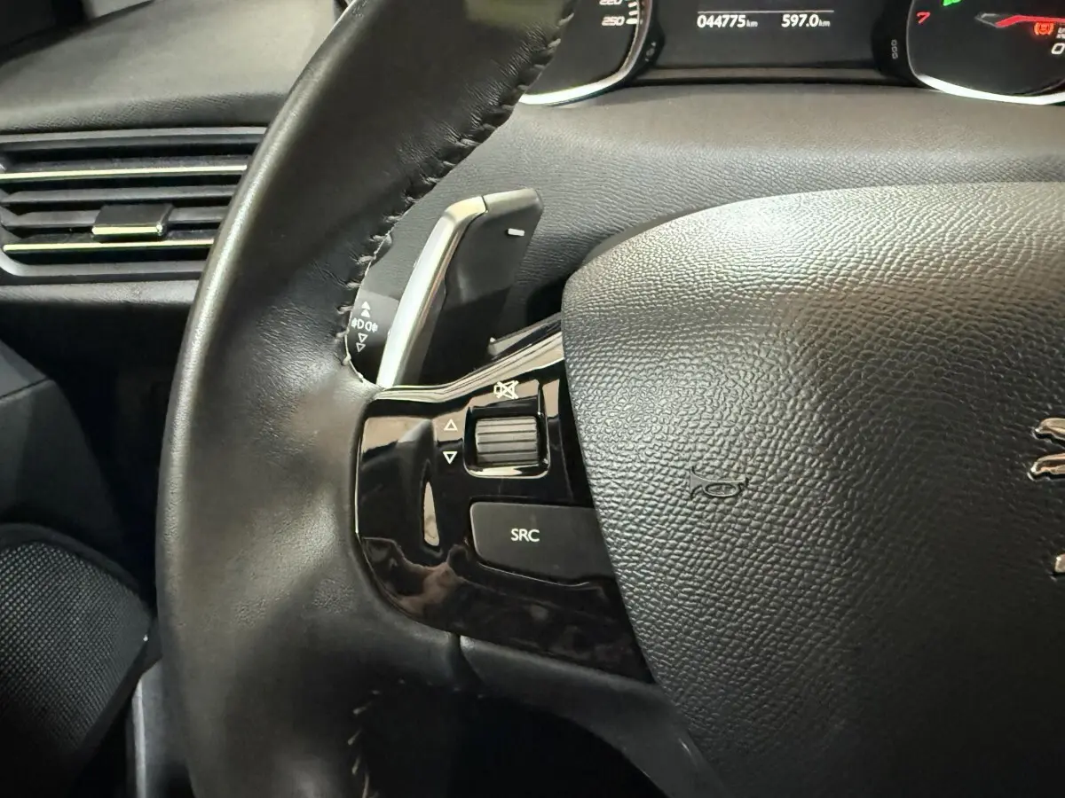 Gros plan sur le volant cuir noir de la Peugeot 308 Puretech 130, avec commandes audio intégrées côté gauche.