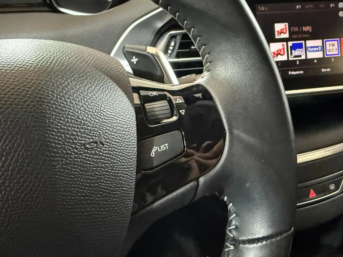 Gros plan sur le volant cuir noir de la Peugeot 308 2020 avec commandes intégrées et écran tactile en arrière-plan.