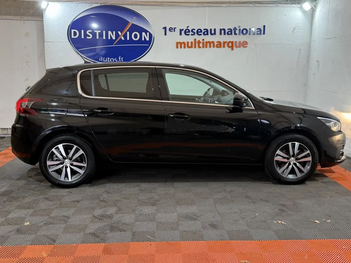 Profil latéral droit d'une Peugeot 308 noire de 2020, avec jantes alliage et vitres teintées, en intérieur showroom.