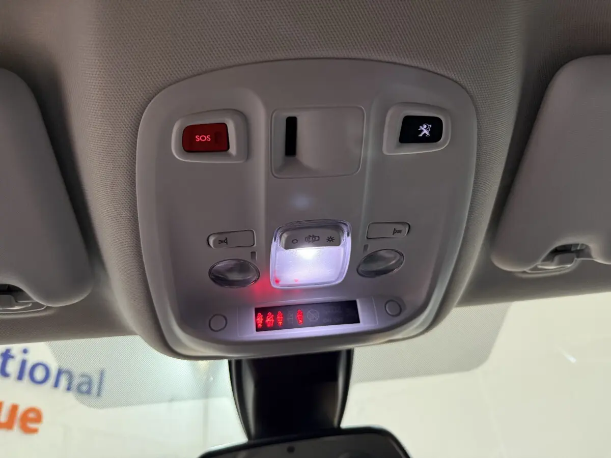 Vue en contre-plongée du plafonnier gris clair avec boutons SOS et logo Peugeot éclairés dans une Peugeot 308 noire.