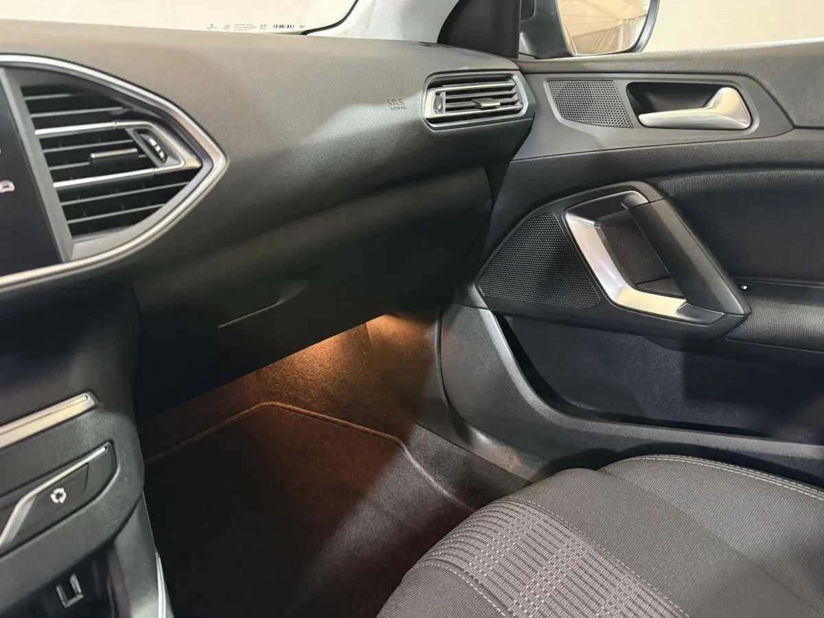 Vue intérieure côté passager de la Peugeot 308 noire 2020, montrant tableau de bord et porte avec éclairage d'ambiance au sol.