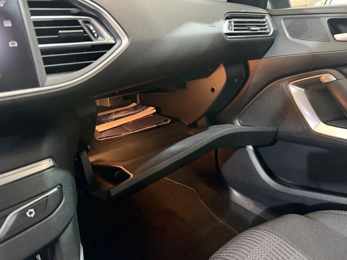 Intérieur côté passager d'une Peugeot 308 noire, boîte à gants ouverte avec documents visibles.
