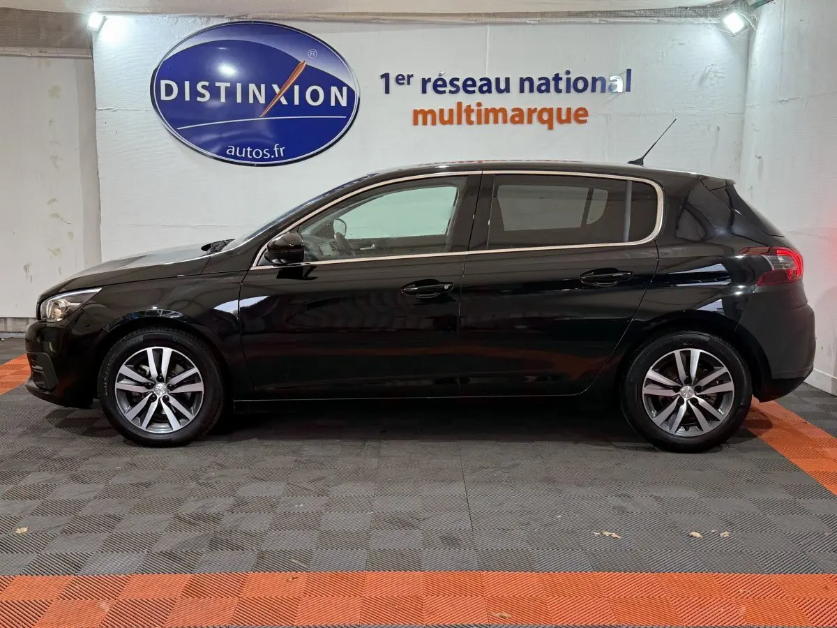 Profil côté gauche d'une Peugeot 308 noire Puretech 130 Allure 2020 dans un showroom avec logo Distinxion en arrière-plan.