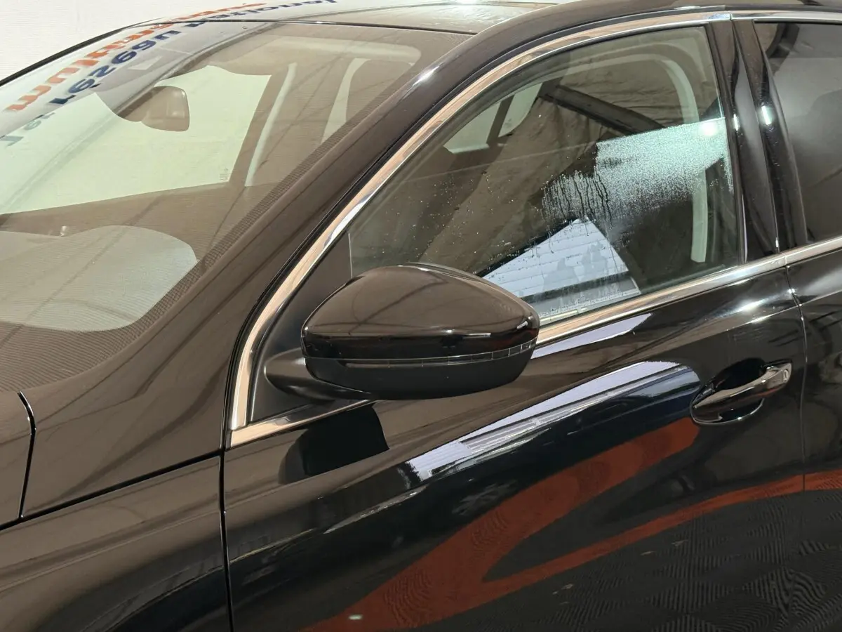 Vue côté gauche rapprochée d'une Peugeot 308 noire 2020, mettant en valeur la portière et le rétroviseur extérieur brillant.