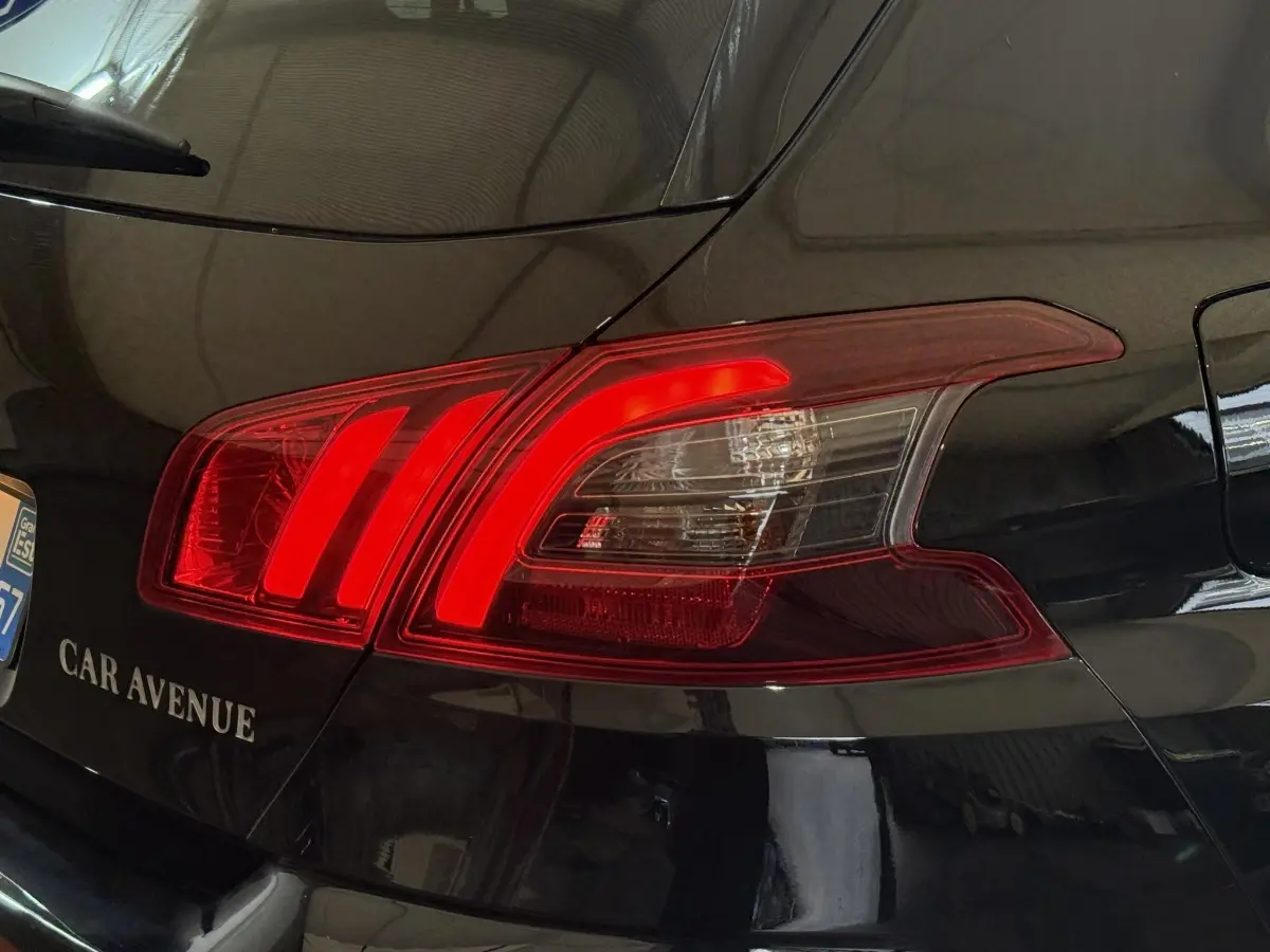 Gros plan sur le feu arrière droit rouge d’une Peugeot 308 noire, avec reflet de l’environnement intérieur visible.