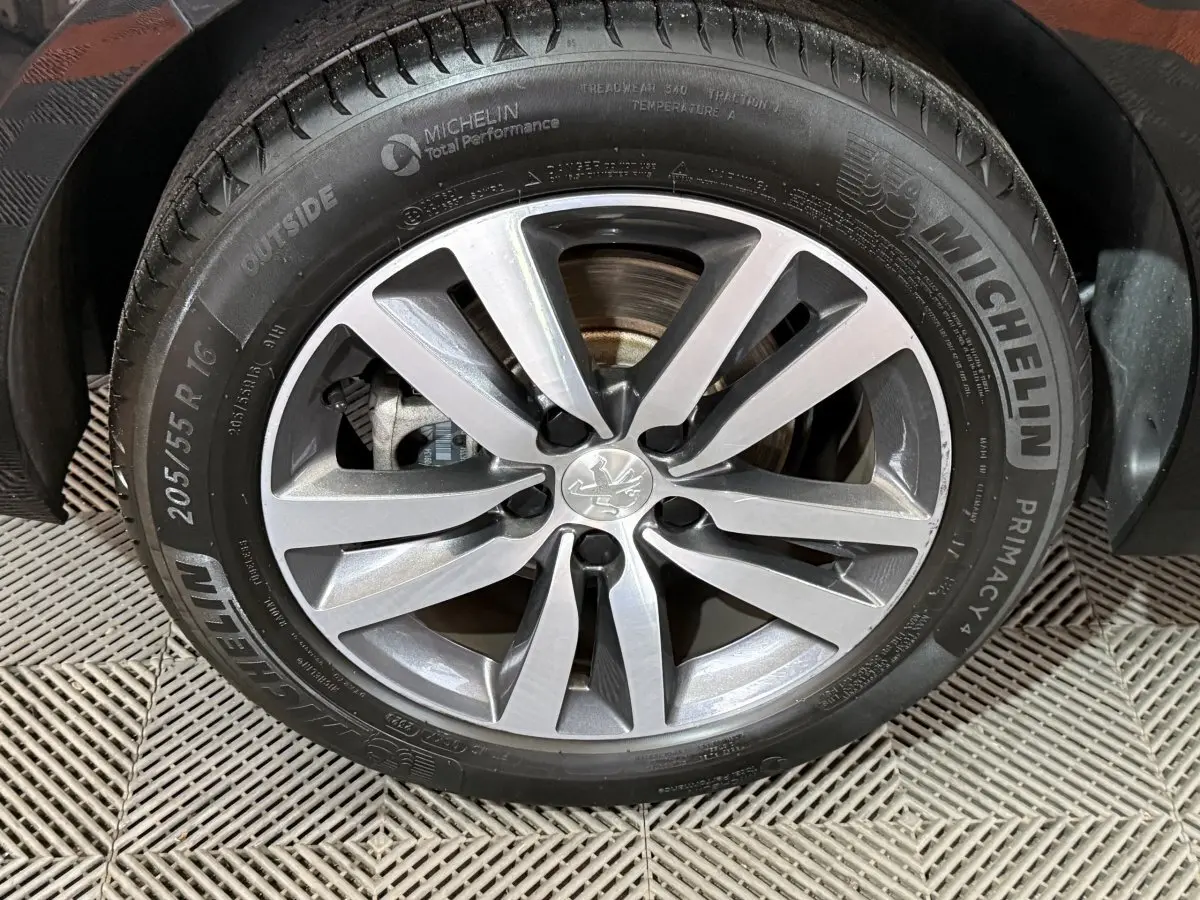 Gros plan sur la roue avant droite de la Peugeot 308 noire, mettant en valeur la jante alliage et le pneu Michelin.