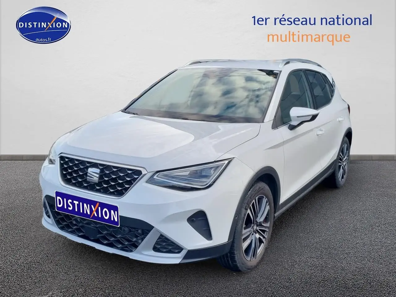 Vue 3/4 avant droite d'un SEAT Arona blanc 2023 avec jantes alu et barres de toit visibles.