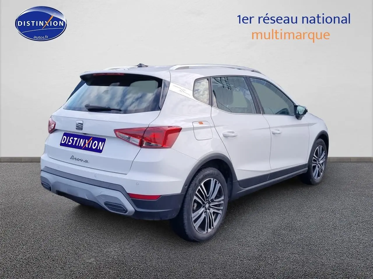 Vue 3/4 arrière droite d’un SEAT Arona blanc avec jantes alu et barres de toit sur fond neutre.