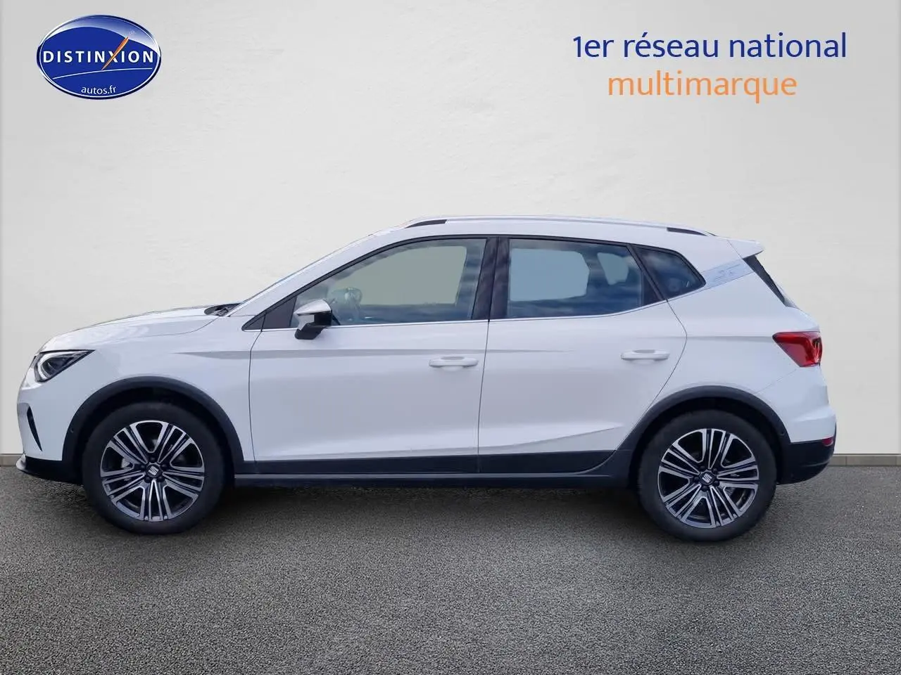 Vue latérale gauche d'un SEAT Arona blanc 2023 avec jantes alliage et barres de toit noires.