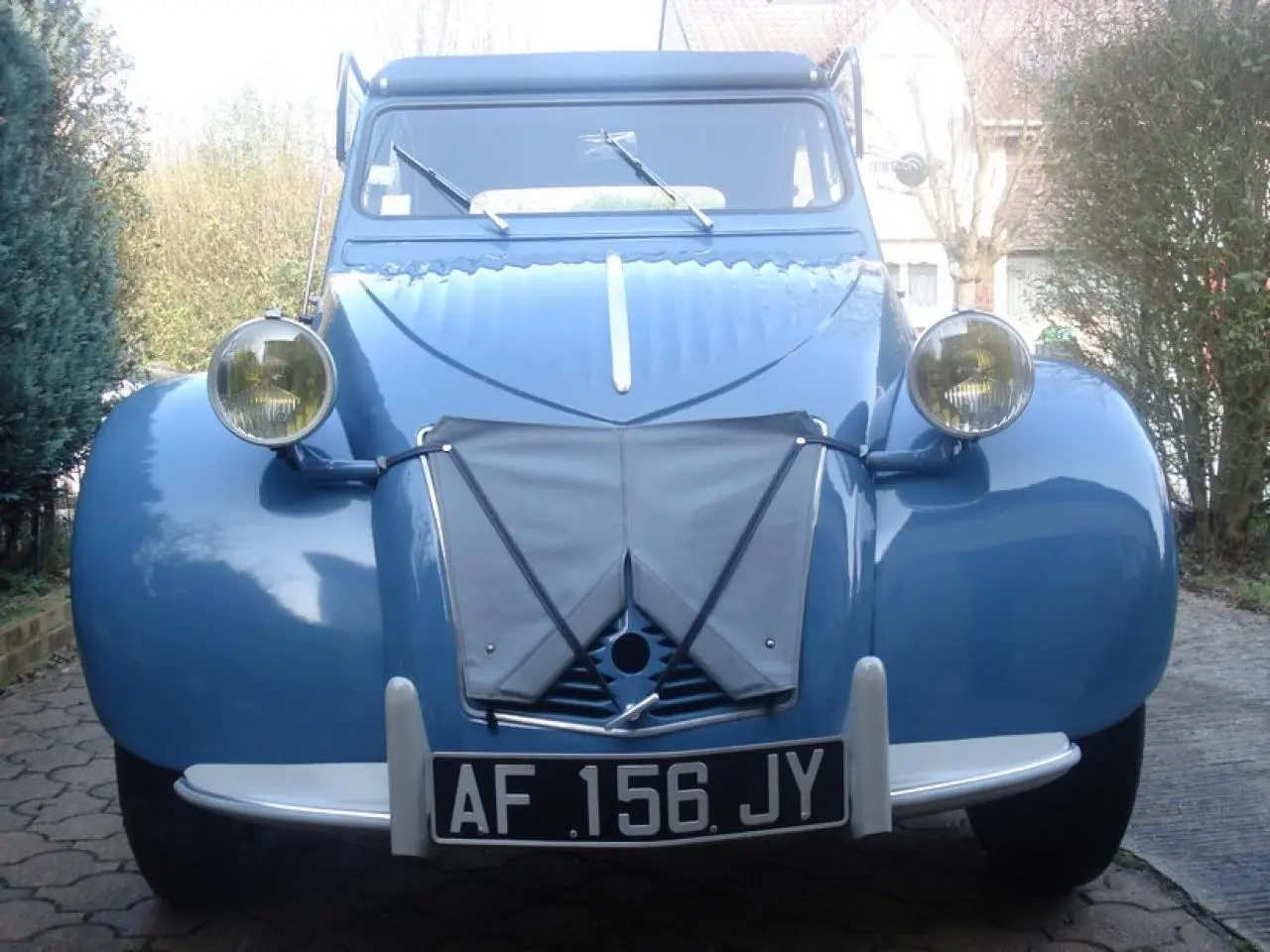 Vue avant d'une Citroën 2 CV bleu clair de 1960 avec ses phares ronds jaunes et sa plaque d'immatriculation noire.