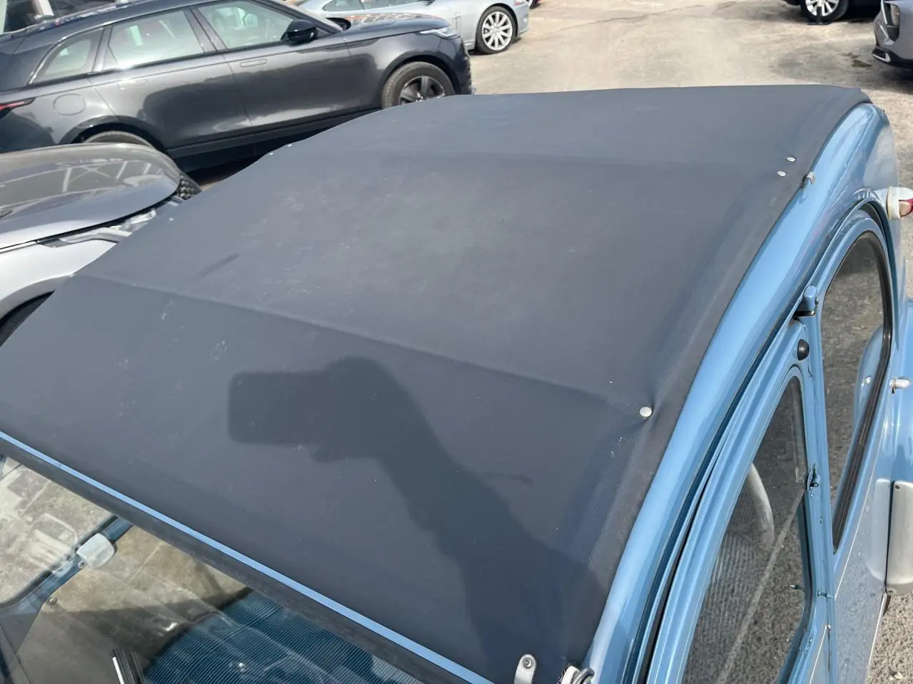 Vue 3/4 avant droit d'une Citroën 2CV bleu clair de 1960 avec toit en toile noir relevé.