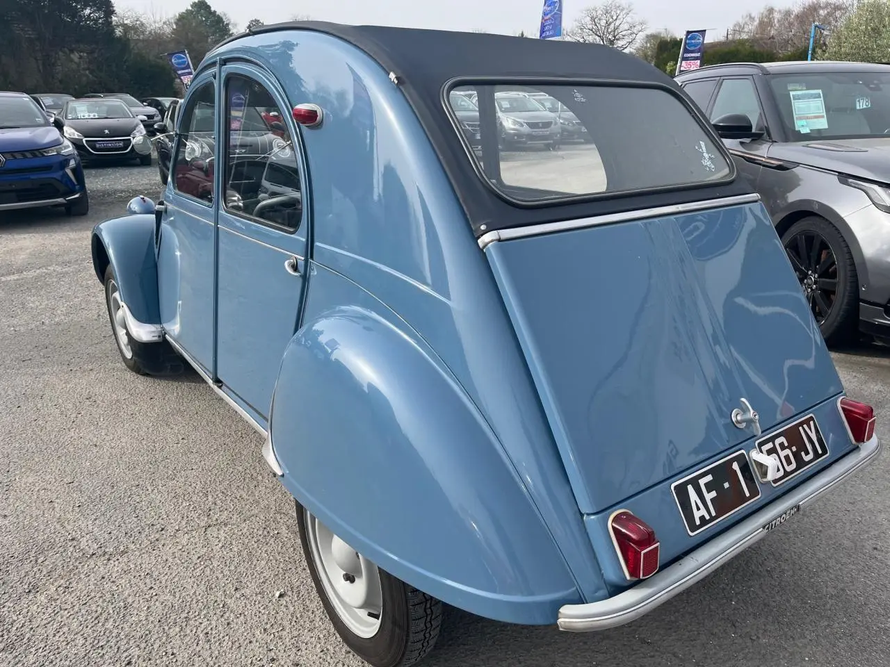 Vue 3/4 arrière d'une Citroën 2 CV bleu clair de 1960 avec toit souple noir et plaques d'immatriculation noires.