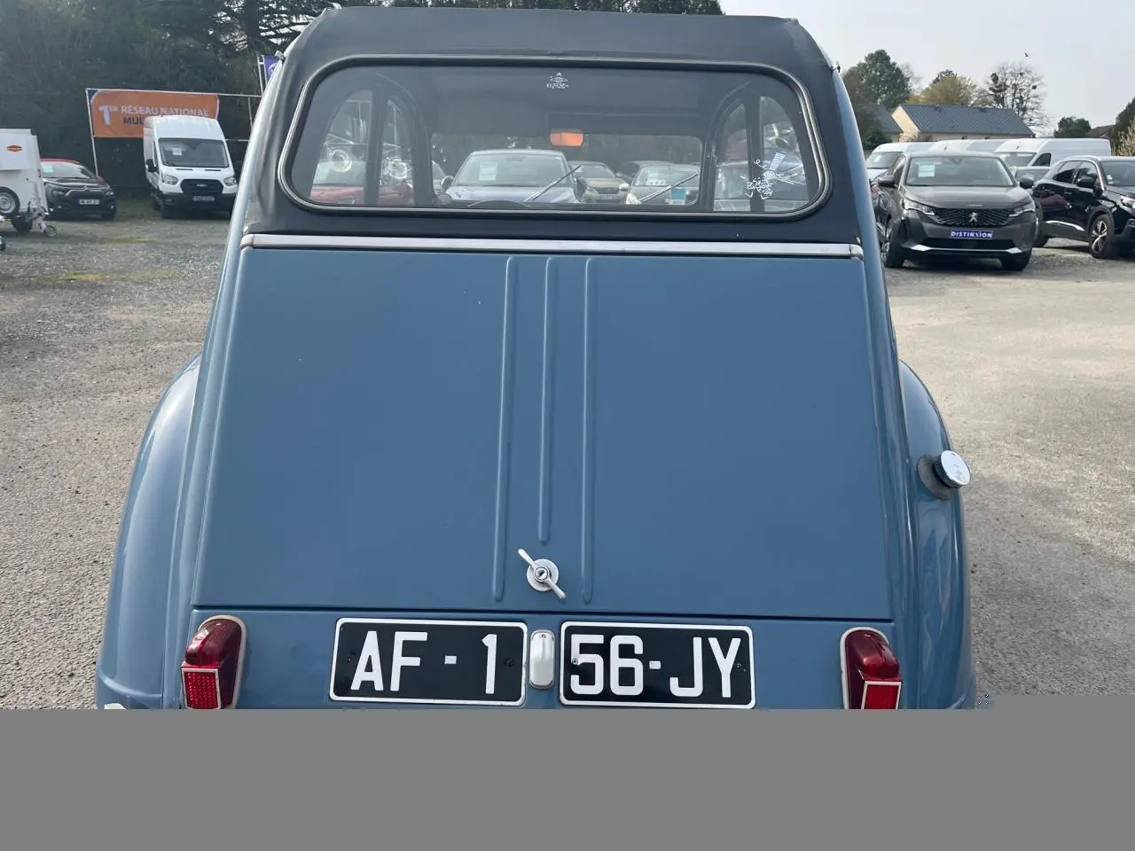 Vue arrière d'une Citroën 2 CV bleu clair de 1960, avec capote noire et plaques d'immatriculation noires.