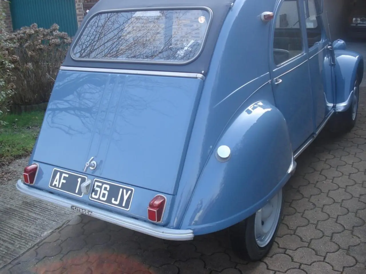 Vue 3/4 arrière droite d'une Citroën 2CV bleu clair de 1960 avec plaques noires et feux arrière rectangulaires rouges.