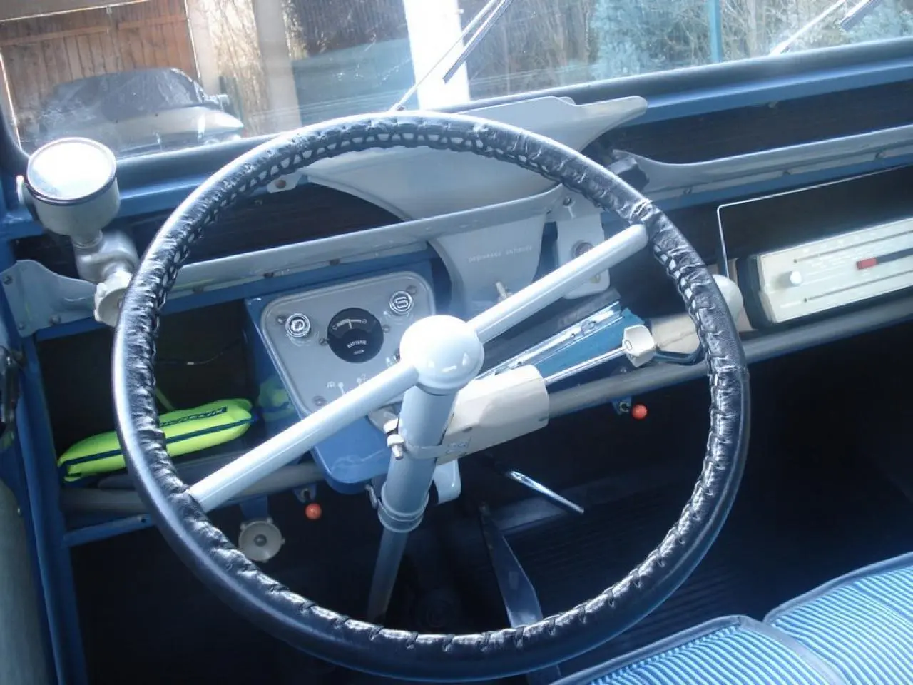 Vue intérieure centrée sur le volant noir et le tableau de bord bleu clair de la Citroën 2 CV de 1960.