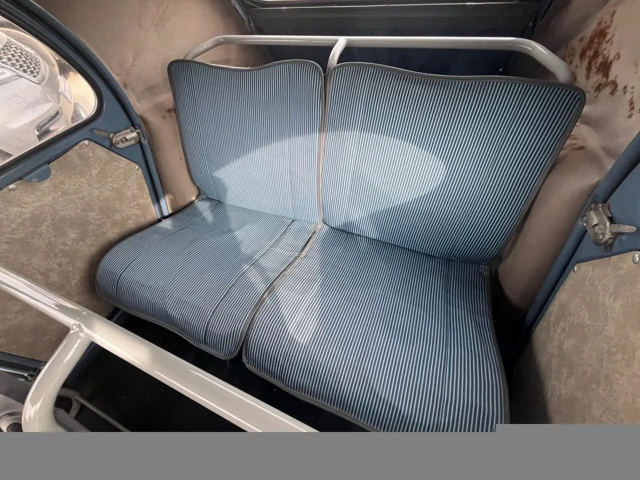 Vue intérieure du siège arrière rayé bleu clair de la Citroën 2 CV de 1960 avec structure métallique blanche visible.