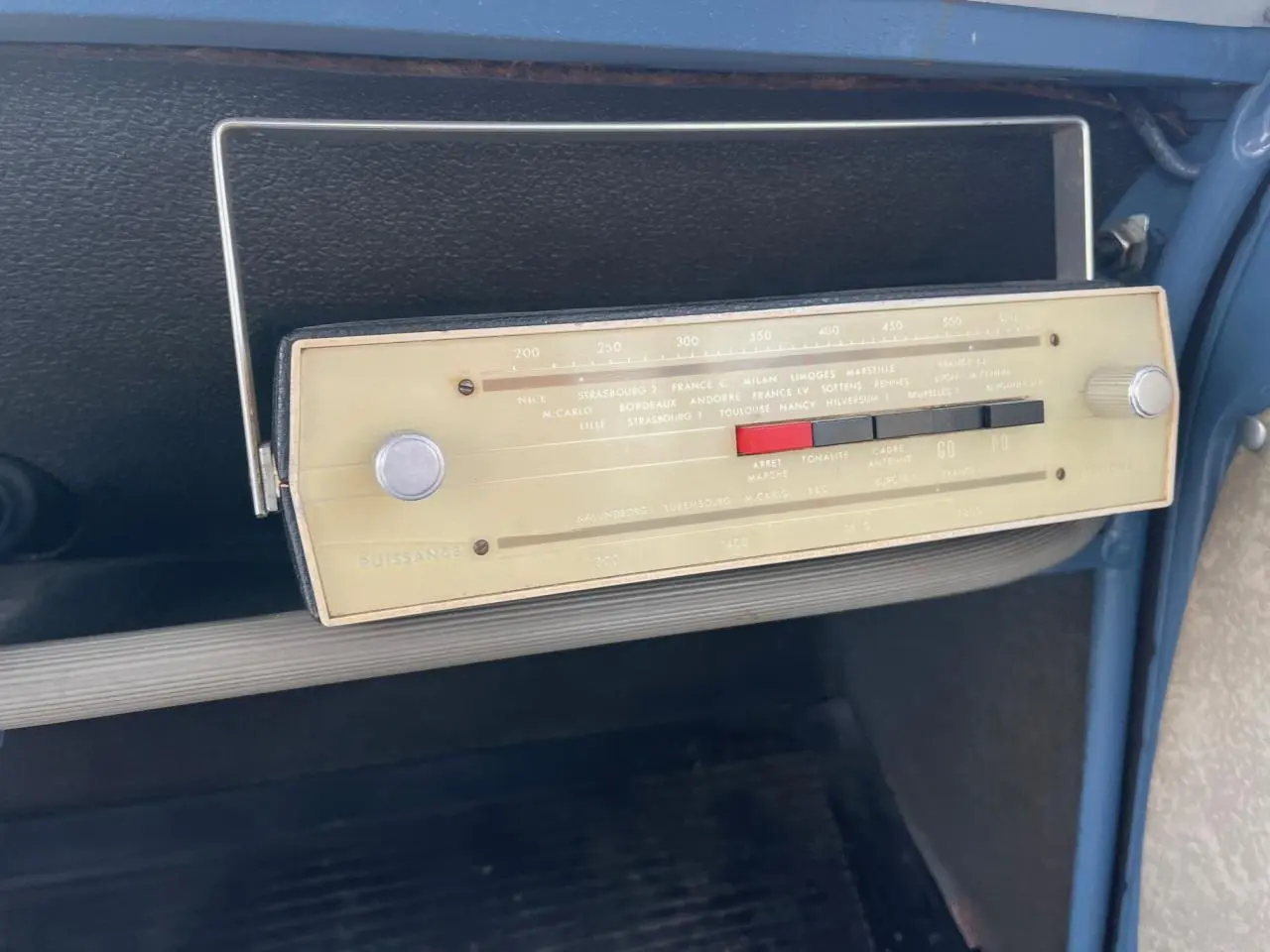 Gros plan sur la radio vintage beige du tableau de bord bleu clair d'une Citroën 2CV de 1960.
