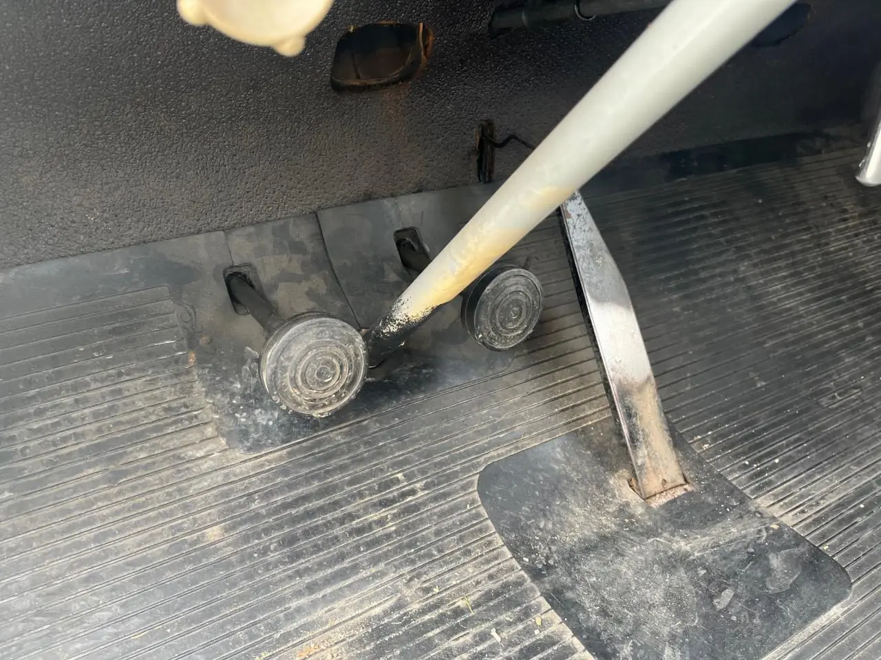 Gros plan sur les pédales et le levier de vitesse gris d'une Citroën 2 CV bleu clair de 1960, intérieur usé et poussiéreux.