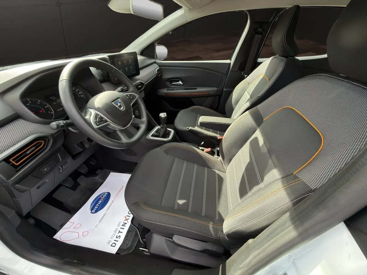 Vue intérieure côté conducteur de la Dacia Sandero Stepway 2022, sièges tissu noir avec surpiqûres orange et volant multifonctions.