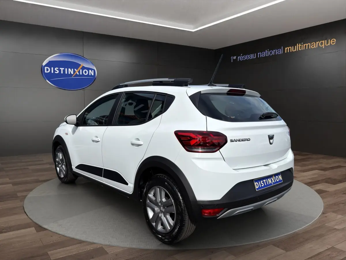 Vue 3/4 arrière droite d'une Dacia Sandero Stepway blanche avec barres de toit et jantes alliage en showroom.