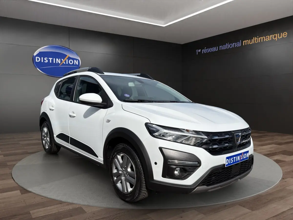 Dacia Sandero Stepway blanc vue 3/4 avant droit avec barres de toit et détails noirs contrastants.
