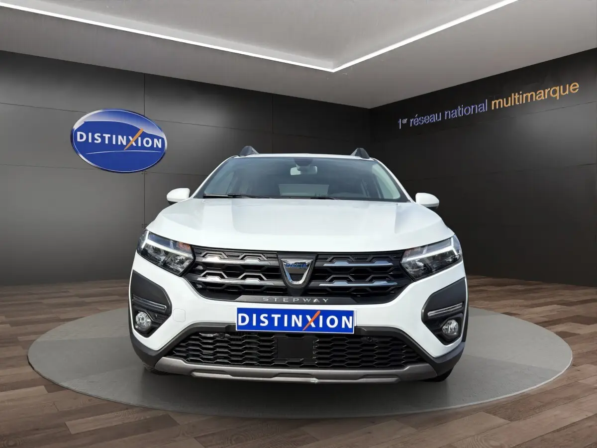 Vue de face d'une Dacia Sandero Stepway blanche avec calandre noire et phares LED dans un showroom.