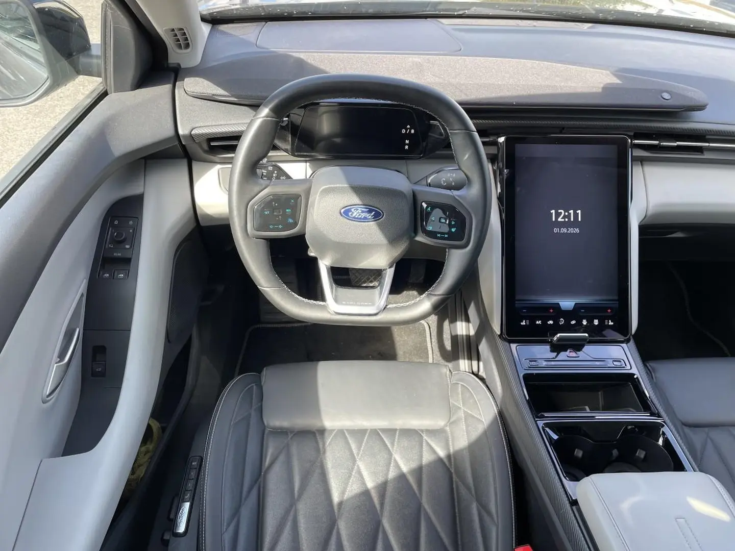 Vue intérieure frontale du Ford Explorer 2025 gris, avec volant multifonction et grand écran tactile vertical central.