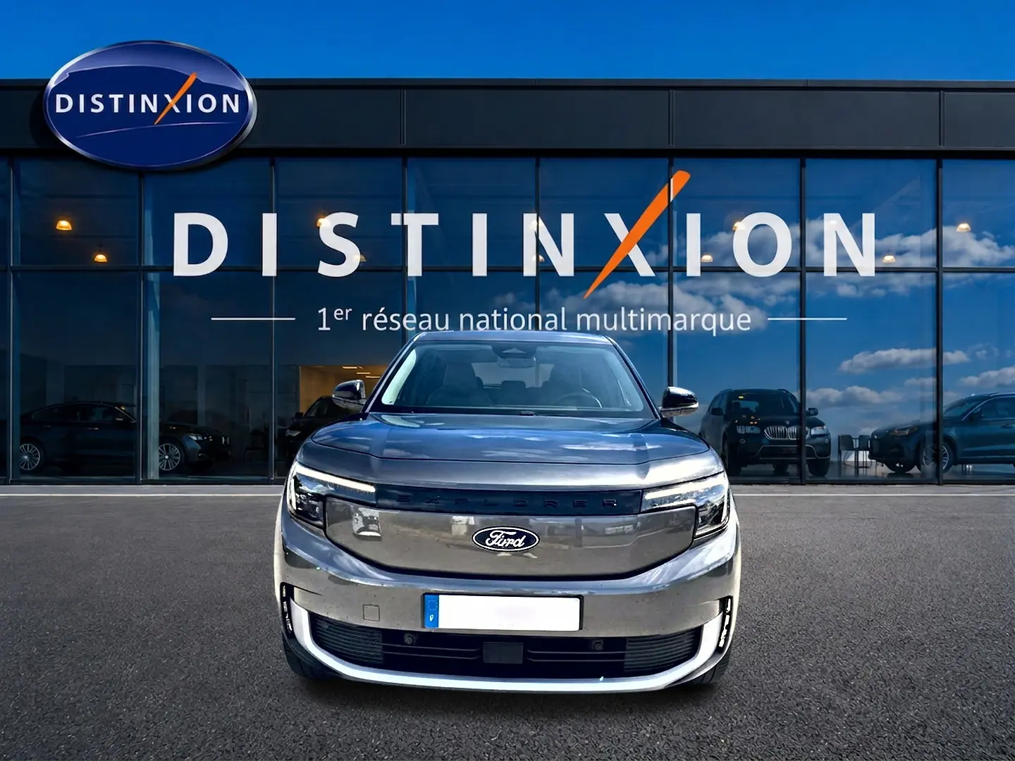 Vue frontale d'un Ford Explorer électrique gris métallisé garé devant une vitrine avec logo Distinxion.