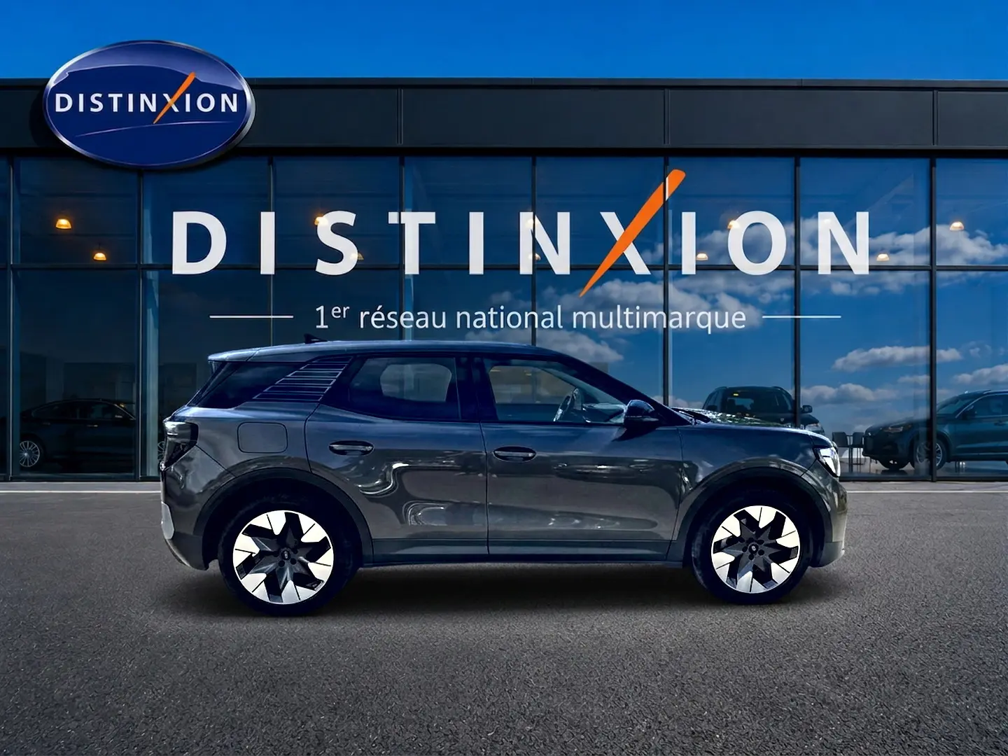 Vue de profil côté gauche d'un Ford Explorer gris électrique 2025, avec jantes alu distinctives, devant une vitrine Distinxion.