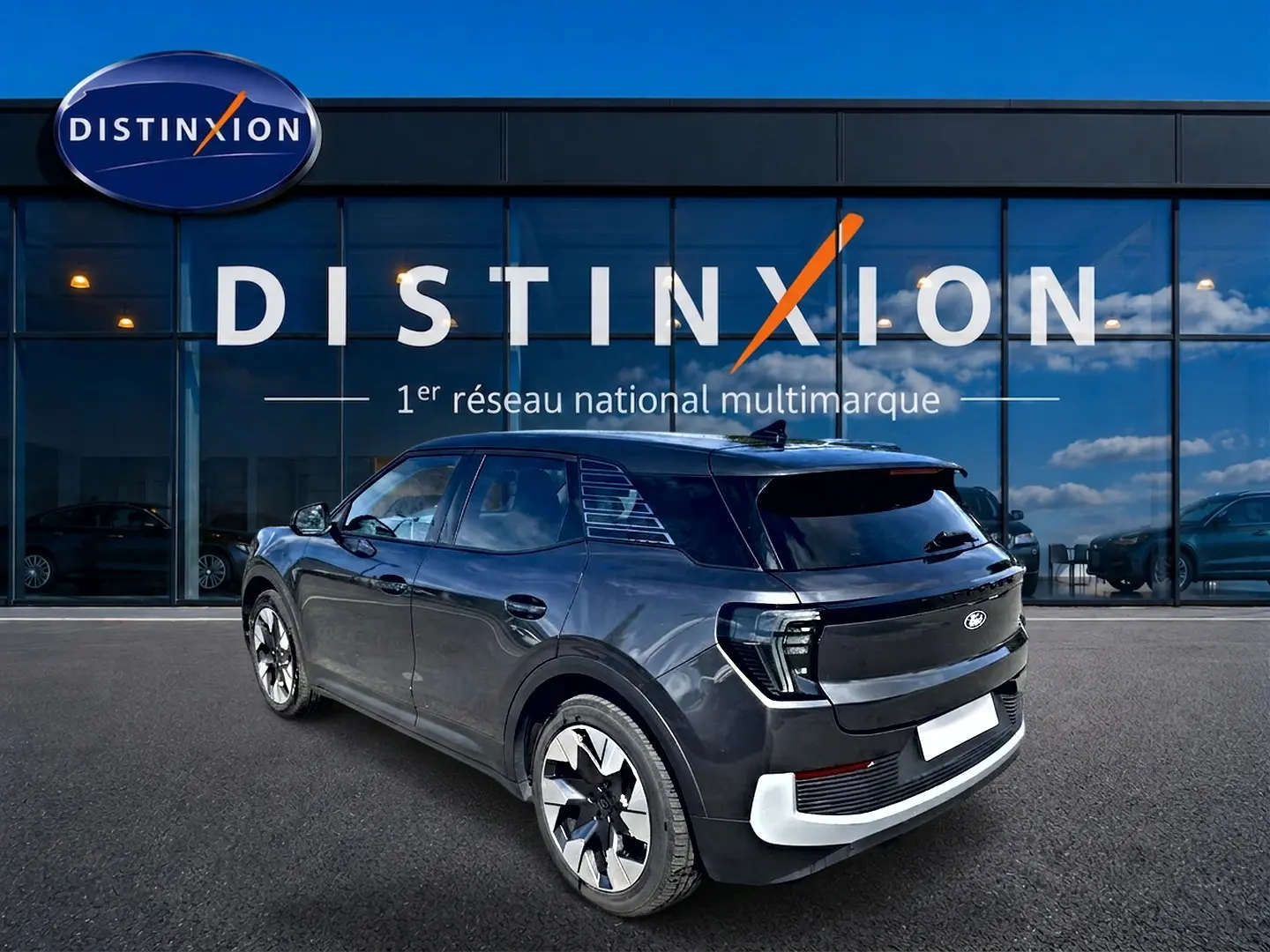 Vue 3/4 arrière droite du Ford Explorer électrique gris, avec jantes alu et vitres arrière surteintées, devant une vitrine Distinxion.