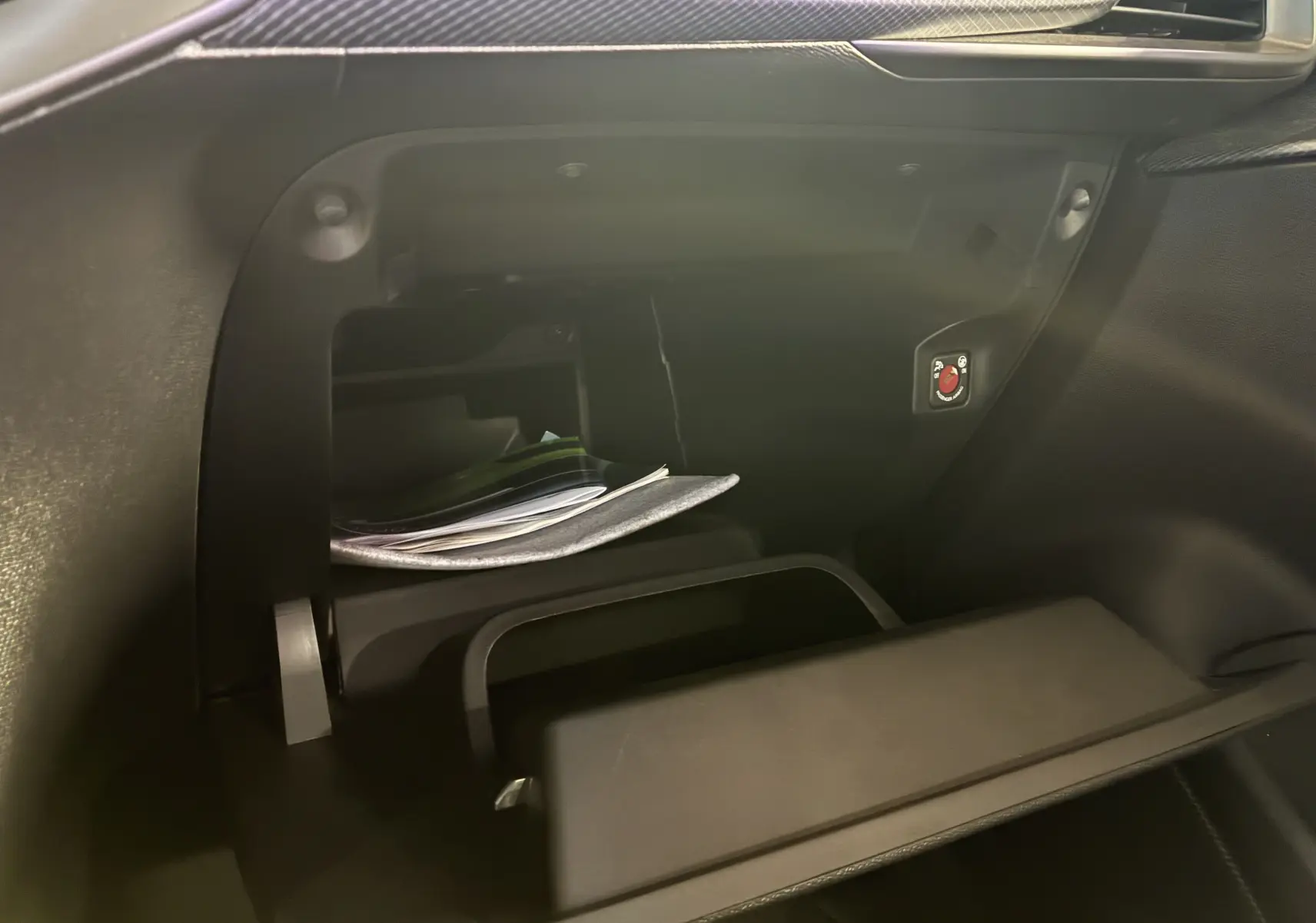 Vue intérieure du vide-poche passager ouvert de l'Opel Mokka 2025 noir, montrant des documents et un bouton rouge distinctif.