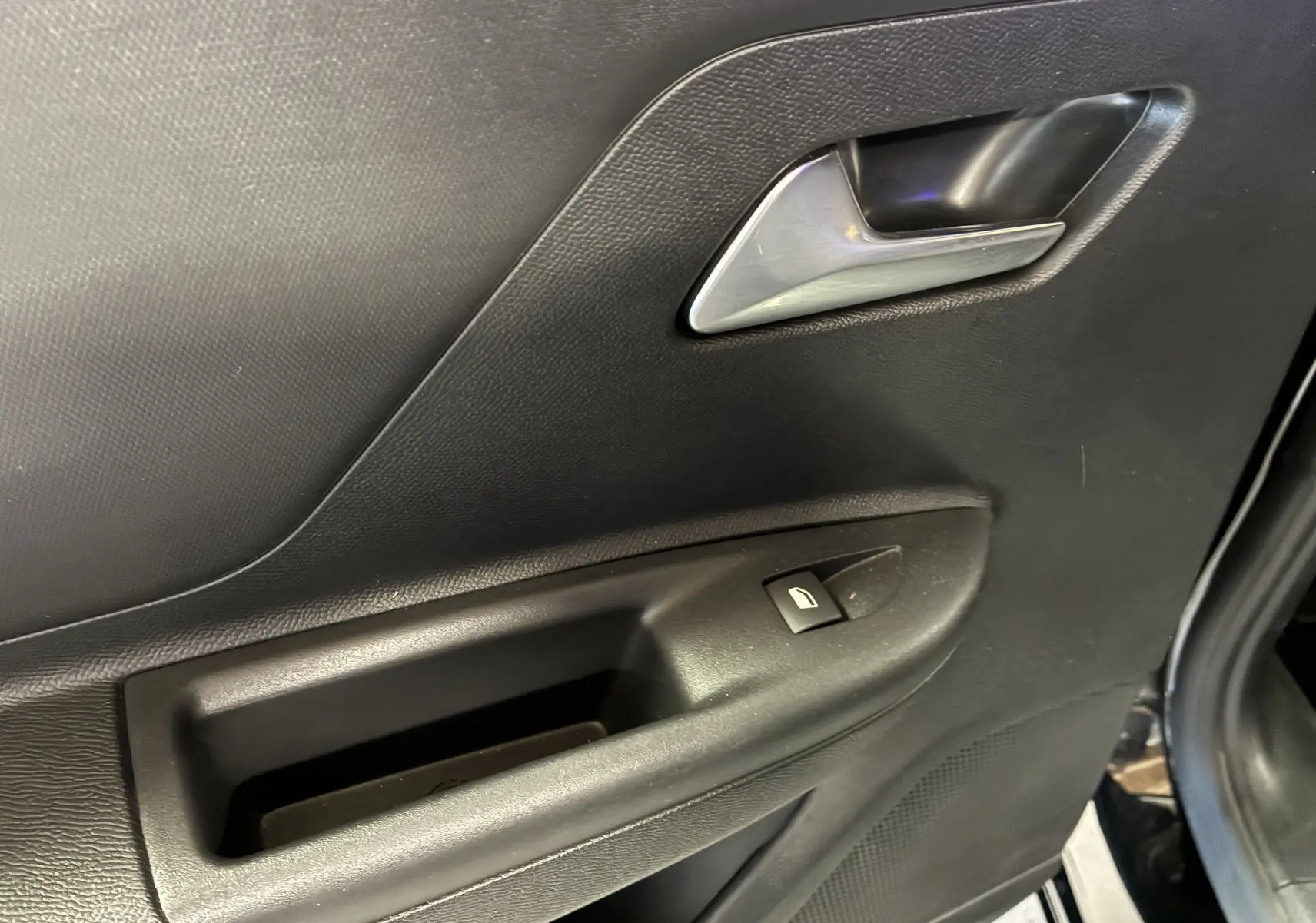 Détail de la porte intérieure côté droit de l'Opel Mokka 2025 noire, avec poignée argentée et bouton de lève-vitre.