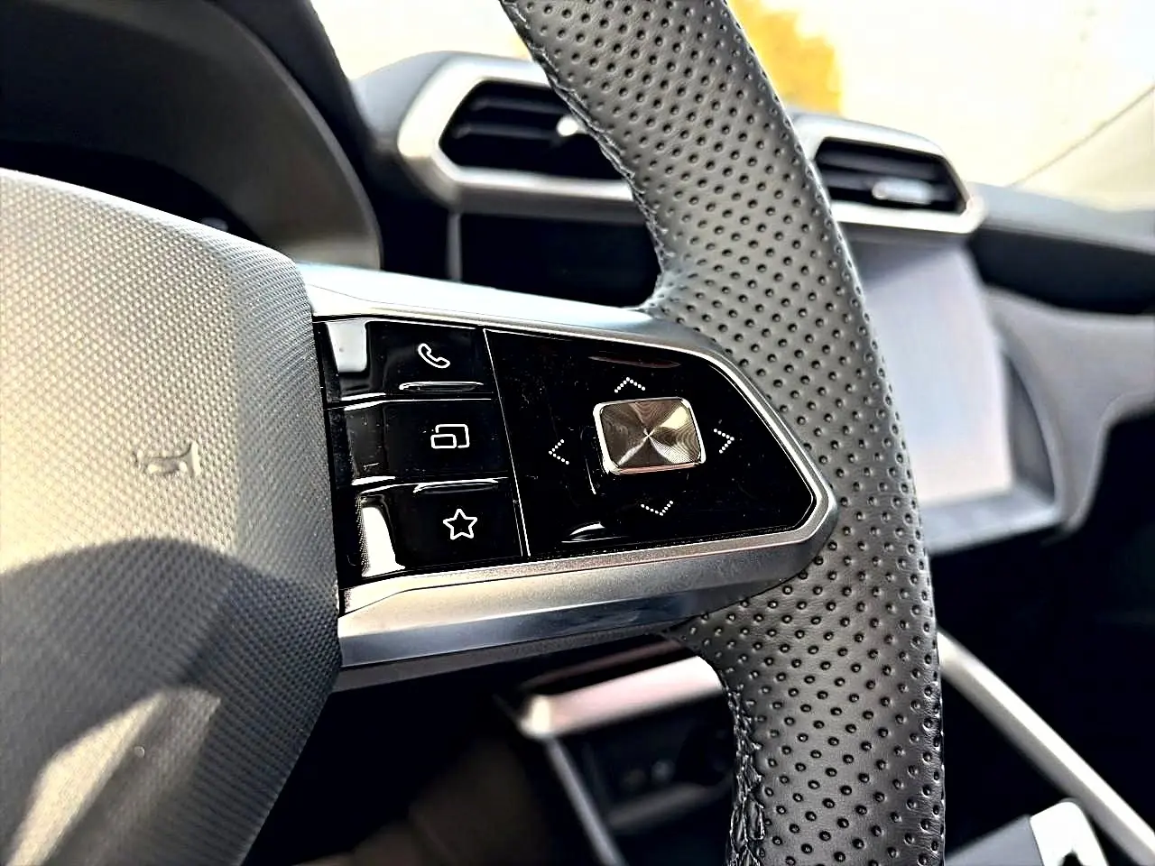 Gros plan sur les commandes au volant perforé du MG Motor ZS 1.5 hybrid 197 Cosmic Silver, tableau de bord en arrière-plan.