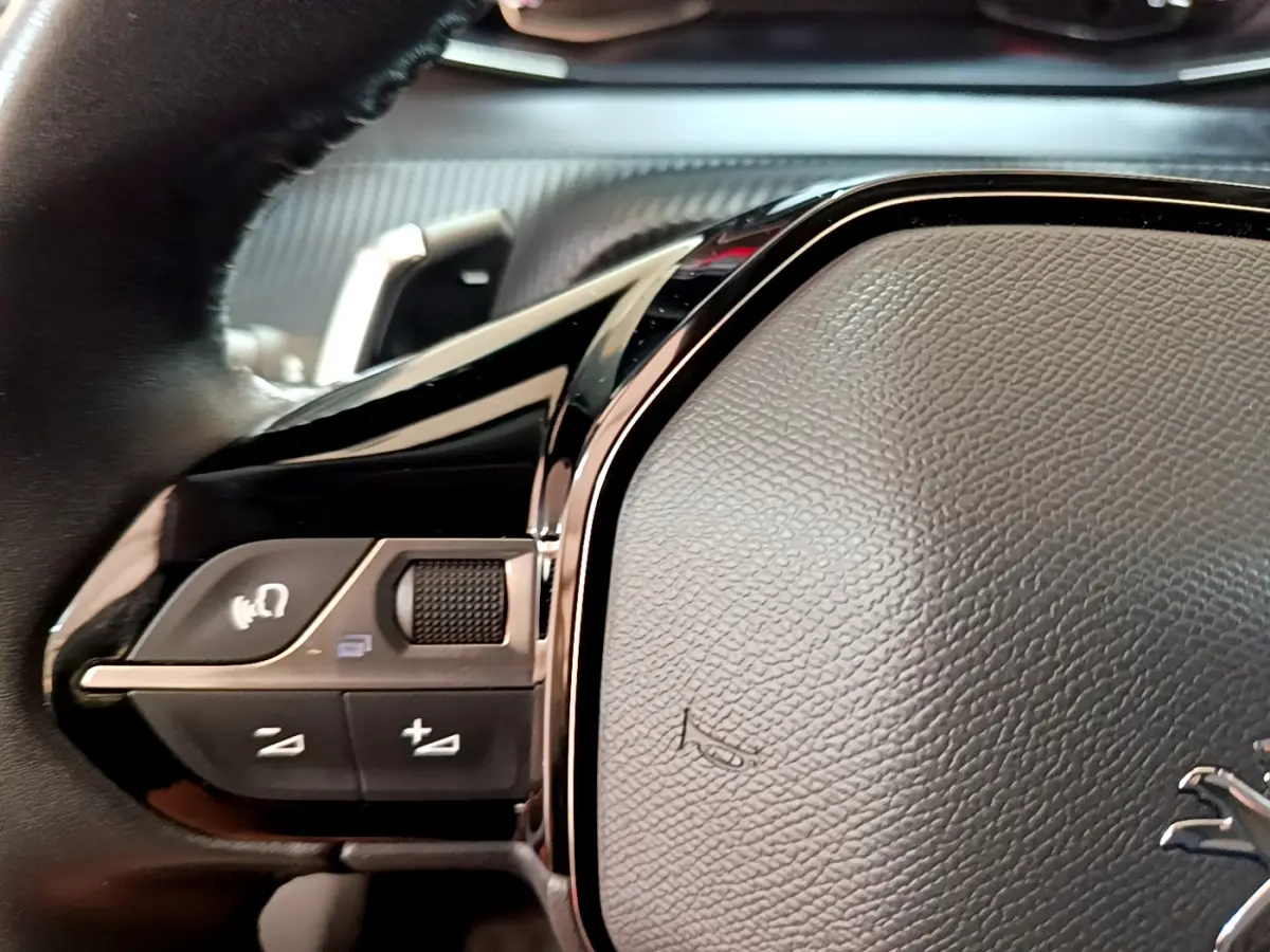 Gros plan sur les commandes gauche du volant cuir noir du Peugeot 2008 gris foncé version Allure 2022.