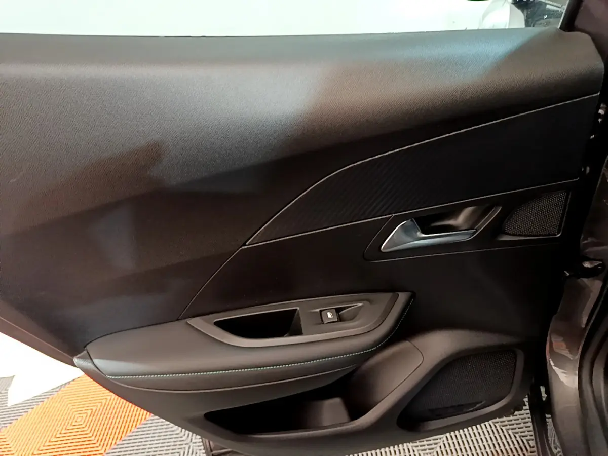Intérieur côté gauche de la porte d'une Peugeot 2008 gris foncé, avec poignée argentée et garniture noire élégante.