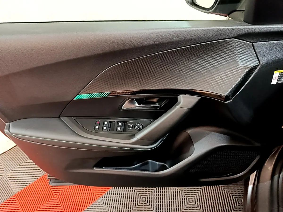 Vue rapprochée de la porte avant gauche du Peugeot 2008 gris foncé avec garniture effet carbone et commandes électriques.
