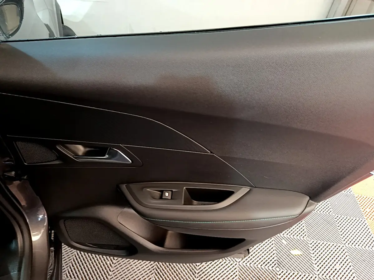 Détail de la porte côté gauche intérieure du Peugeot 2008 gris foncé, avec commandes de vitre et poignée intégrée.