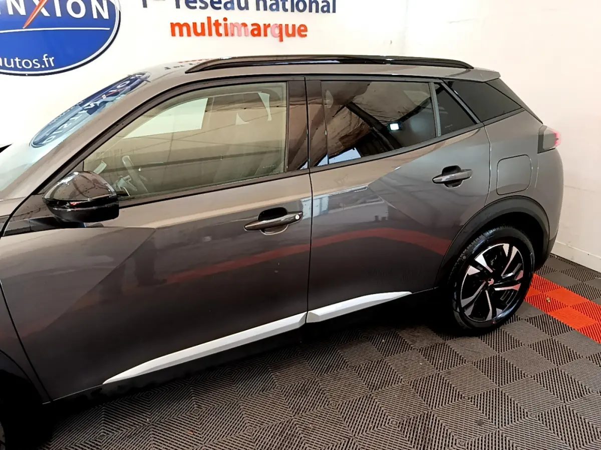 Profil droit d'un Peugeot 2008 gris foncé avec jantes noires et toit noir en intérieur showroom.