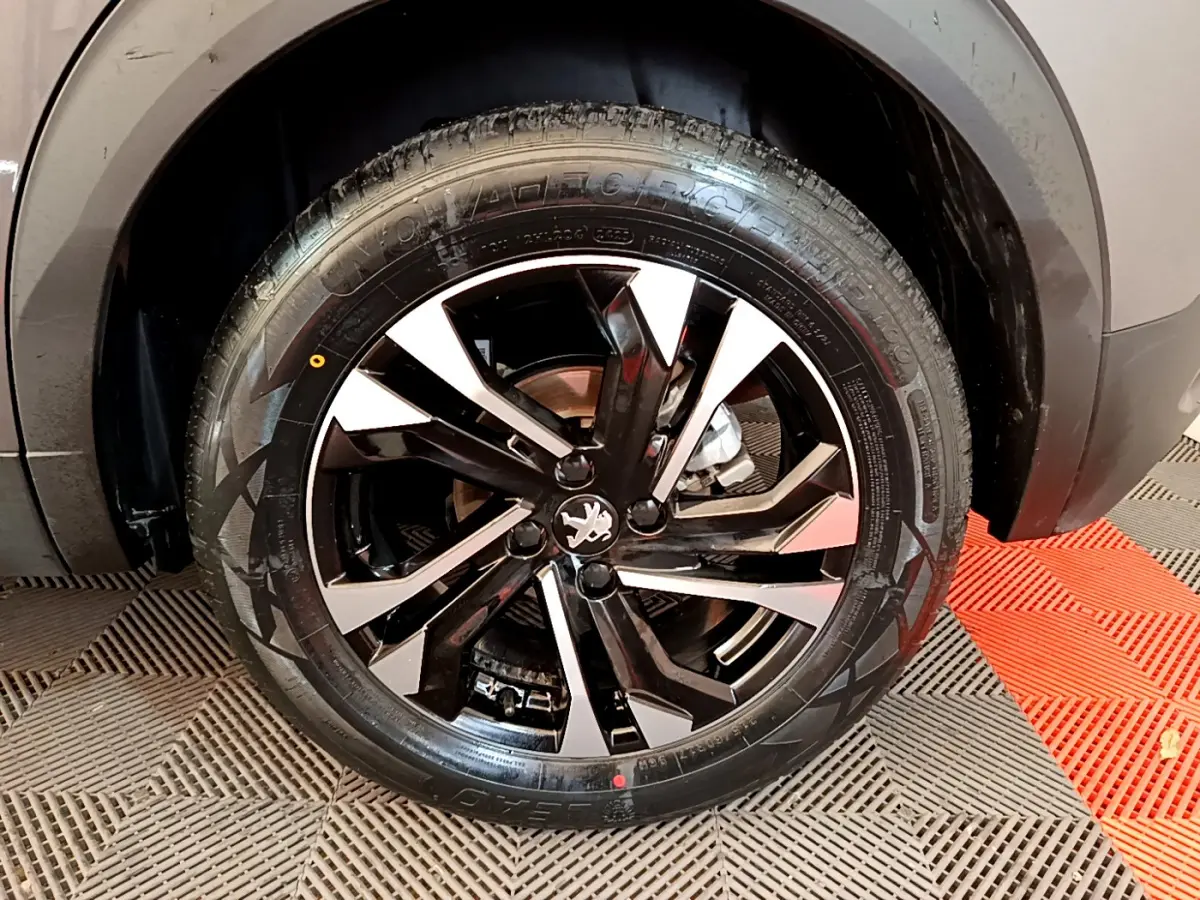 Gros plan sur la roue avant droite du Peugeot 2008 gris foncé, mettant en valeur la jante alliage noire et argentée.