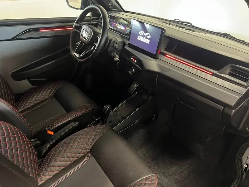 Vue intérieure côté conducteur de la Ligier JS50 Sport Ultimate E5+ 2025, sièges noirs avec surpiqûres rouges et écran tactile central.