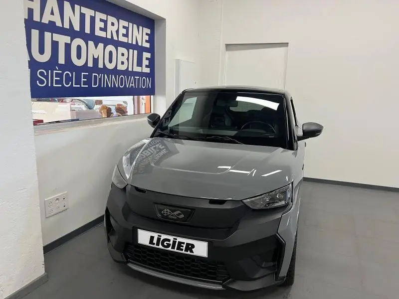 Vue avant d'une Ligier JS50 Sport Ultimate E5+ gris avec calandre noire et toit noir dans un showroom.