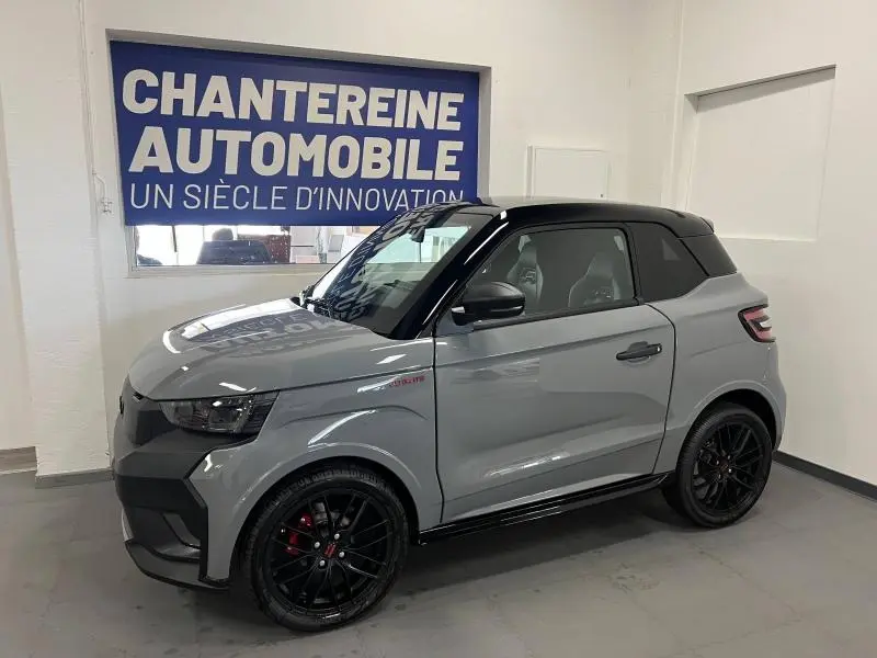 Vue 3/4 avant droit d'une Ligier JS50 Sport Ultimate E5+ gris avec toit noir et jantes noires en intérieur showroom.