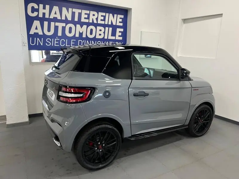 Vue 3/4 arrière droite d'une Ligier JS50 Sport Ultimate E5+ gris avec toit noir et jantes noires en intérieur showroom.