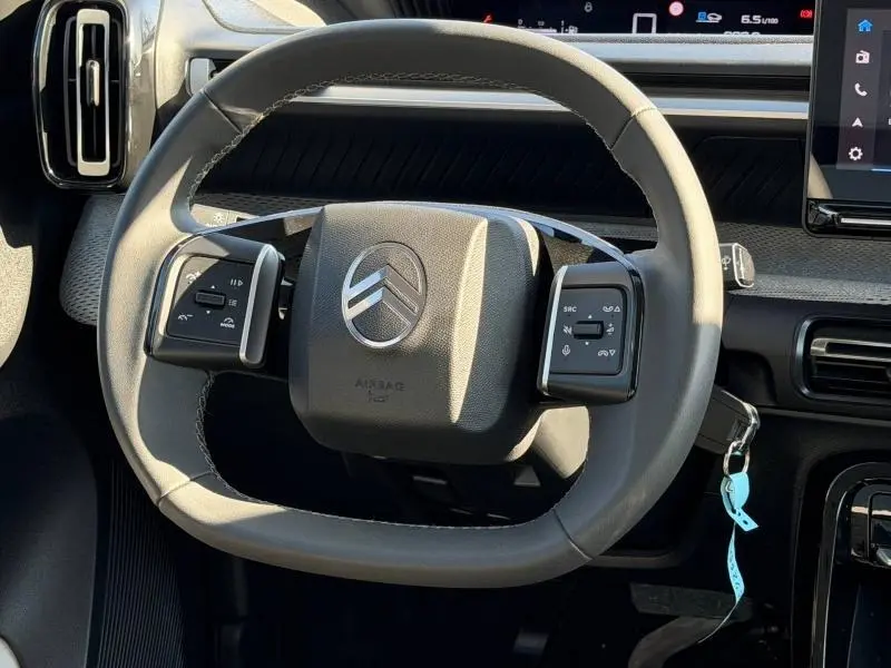 Vue rapprochée du volant gris clair de la Citroën C3 1.2 Turbo 100ch MAX avec commandes intégrées et tableau de bord en arrière-plan.