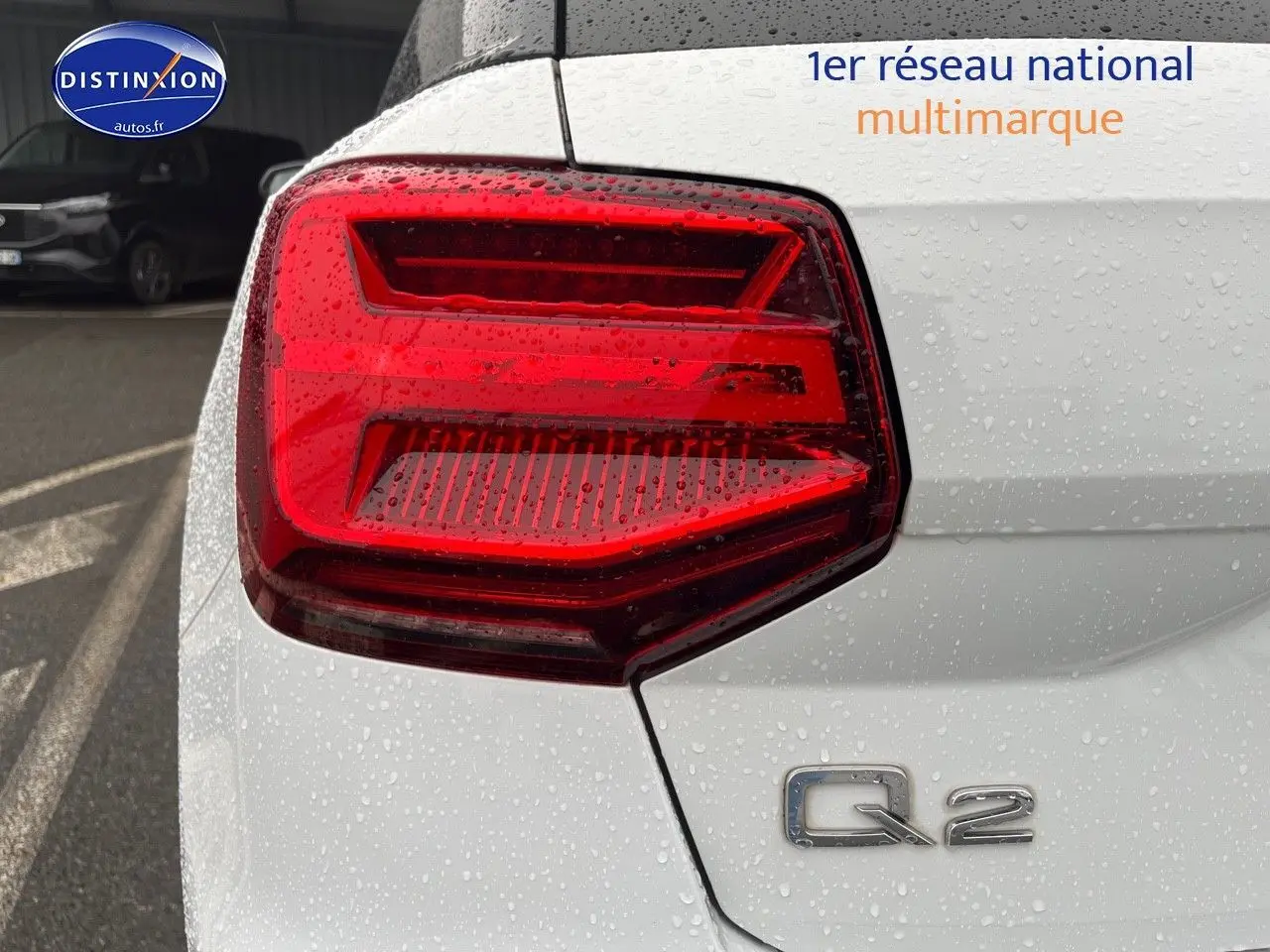 Gros plan sur le feu arrière gauche d’un Audi Q2 blanc Ibis avec logo Q2 sous la pluie.